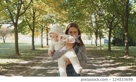 A beautiful and joyful moment captured of a mother lovingly carrying her baby in a picturesque autumn park A beautiful and joyful moment captured of a mother lovingly carrying her baby in a picturesque autumn park 124833699