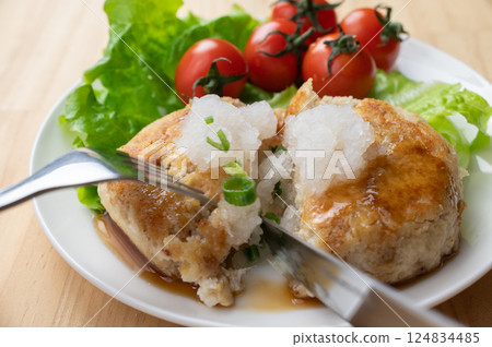 Tofu hamburger served on a white plate is being cut with a fork and knife 124834485