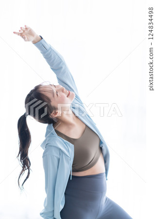A young woman wearing long sleeves stretching in a bright room A young woman wearing long sleeves stretching in a bright room 124834498