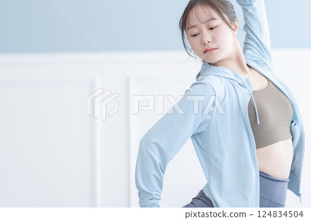 A young woman wearing long sleeves stretching in a bright room 124834504