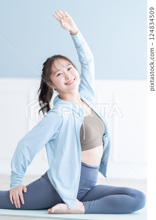 一位身穿長袖的年輕女子在明亮的房間裡伸展身體 124834509