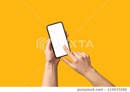 Hands interact with a modern smartphone against a vibrant yellow background Hands interact with a modern smartphone against a vibrant yellow background 124835098