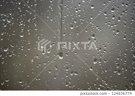 Window covered in glistening raindrops creates a soothing and textured background on a rainy day. 124836774