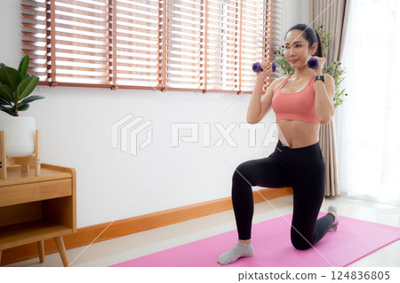 Young asian woman in sportswear workout with dumbbells for strength in living room at home. 124836805
