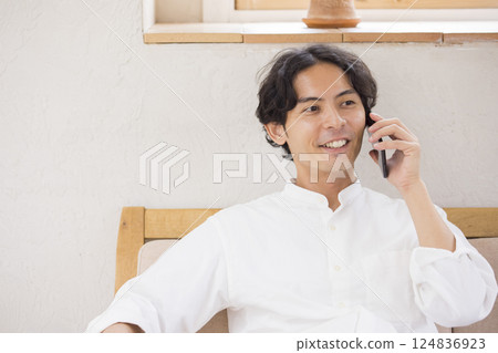 A young man sitting on a sofa and talking on a smartphone 124836923