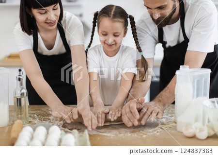 Caucasian father, mother, and daughter cooking in home kitchen, smiling, rolling dough, enjoying family baking fun. Appears cheerful, lively, showcases teamwork and food preparation activity. Caucasian father, mother, and daughter cooking in home kitchen, smiling, rolling dough, enjoying family baking fun. Appears cheerful, lively, showcases teamwork and food preparation activity. 124837383