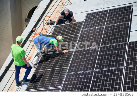 Workers building solar panel system on metal rooftop of house. Three men installers installing photovoltaic solar module outdoors. Alternative, green and renewable energy generation concept. 124838562