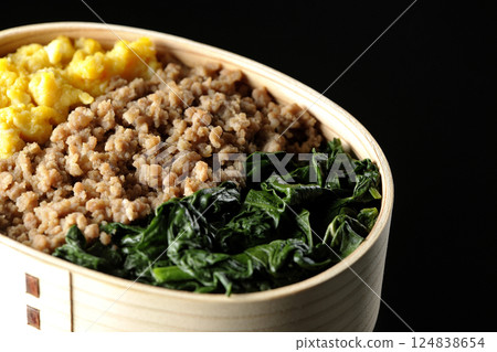 Three-color bento box with egg, meat, and spinach photographed against a black background Three-color bento box with egg, meat, and spinach photographed against a black background 124838654