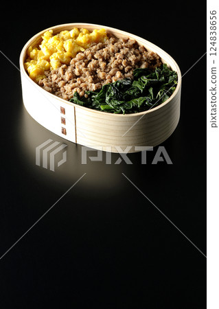 Three-color bento box with egg, meat, and spinach photographed against a black background Three-color bento box with egg, meat, and spinach photographed against a black background 124838656