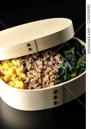 Three-color bento box with egg, meat, and spinach photographed against a black background 124838692