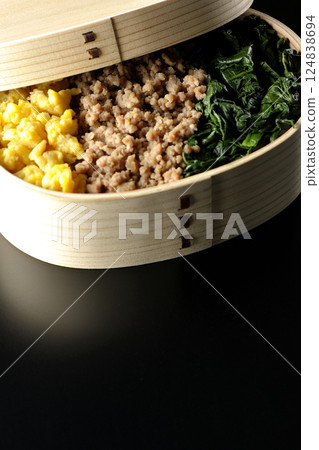 Three-color bento box with egg, meat, and spinach photographed against a black background 124838694