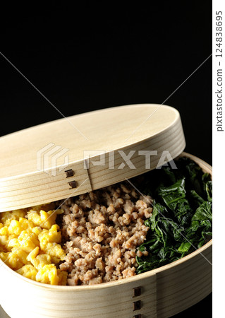 Three-color bento box with egg, meat, and spinach photographed against a black background 124838695
