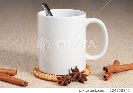 Blank 11oz white mug on the coaster on the table. Mug with spoon, cinnamon, star anise Blank 11oz white mug on the coaster on the table. Mug with spoon, cinnamon, star anise 124838843