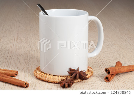 Blank 11oz white mug on the coaster on the table. Mug with spoon, cinnamon, star anise Blank 11oz white mug on the coaster on the table. Mug with spoon, cinnamon, star anise 124838845