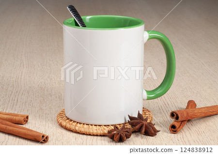 Two-tone 11oz mug on the mug coaster on the table. Mug with spoon, cinnamon, star anise. Mug with green handle and inner part. Two-tone 11oz mug on the mug coaster on the table. Mug with spoon, cinnamon, star anise. Mug with green handle and inner part. 124838912