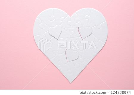 White heart-shaped jigsaw puzzle on a grey background, with several pieces missing and placed nearby. Symbolizing love, connection, or incompleteness, perfect for themes of relationships and emotions. 124838974