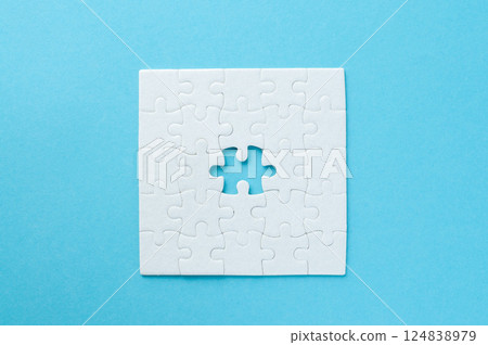 Concept for problem-solving, teamwork, solutions, or missing connections. White jigsaw puzzle on a vibrant blue background with one missing piece. Minimalist composition with copy space. 124838979