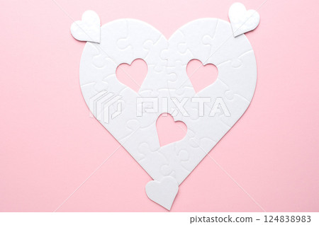 White heart-shaped jigsaw puzzle on a grey background, with several pieces missing and placed nearby. Symbolizing love, connection, or incompleteness, perfect for themes of relationships and emotions. 124838983