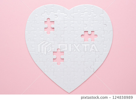 White heart-shaped jigsaw puzzle on a grey background, with several pieces missing and placed nearby. Symbolizing love, connection, or incompleteness, perfect for themes of relationships and emotions. 124838989