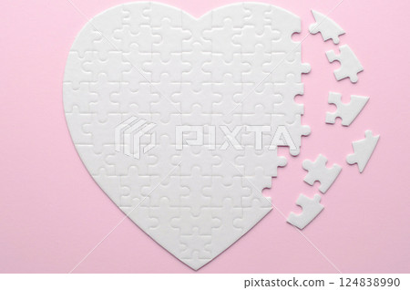 White heart-shaped jigsaw puzzle on a grey background, with several pieces missing and placed nearby. Symbolizing love, connection, or incompleteness, perfect for themes of relationships and emotions. White heart-shaped jigsaw puzzle on a grey background, with several pieces missing and placed nearby. Symbolizing love, connection, or incompleteness, perfect for themes of relationships and emotions. 124838990