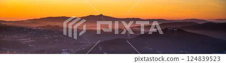 The sun sets behind Jested Ridge, creating a stunning silhouette against the colorful sky. Layers of mist drift over the valleys, enhancing the tranquil atmosphere of this Czech landscape. 124839523