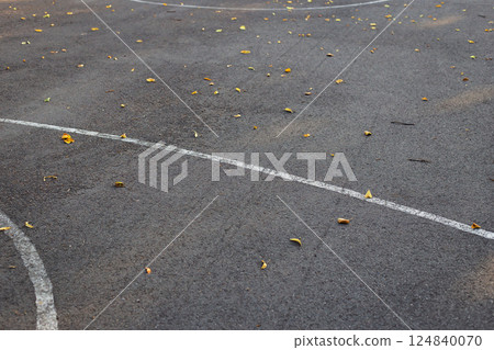 A close-up of an asphalt court with scattered yellow leaves and white lines, signaling the onset of autumn 124840070
