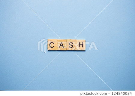Wooden blocks spelling the word 'CASH' on a light blue background 124840084