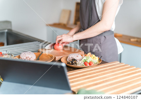 一位身穿圍裙的女士一邊做飯，一邊使用平板電腦上的應用程式查看食譜 124840107