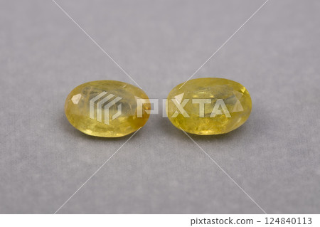 Two sparkling, oval-shaped, faceted natural yellow sphene gemstones displayed on grey textured background Two sparkling, oval-shaped, faceted natural yellow sphene gemstones displayed on grey textured background 124840113