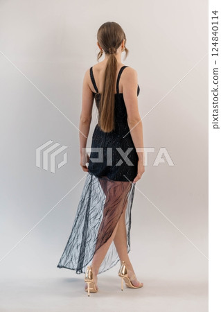 Elegant Young Woman in Stylish Black Sheer Evening Dress and Golden High Heels Posing Gracefully with Back View Elegant Young Woman in Stylish Black Sheer Evening Dress and Golden High Heels Posing Gracefully with Back View 124840114