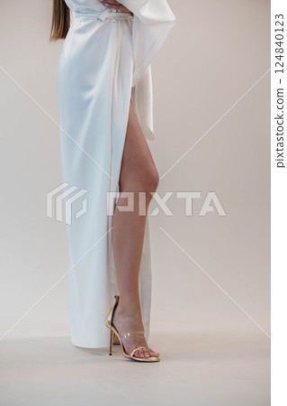 Elegant Female Model Wearing White Satin Dress with High Slit and Gold High Heels in Studio Elegant Female Model Wearing White Satin Dress with High Slit and Gold High Heels in Studio 124840123