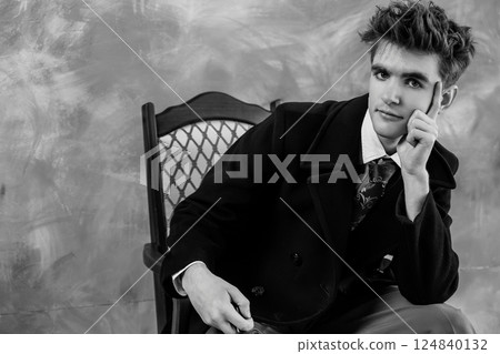 Black and white portrait of a young man in formal attire, leaning on an antique chair with a contemplative expression Black and white portrait of a young man in formal attire, leaning on an antique chair with a contemplative expression 124840132