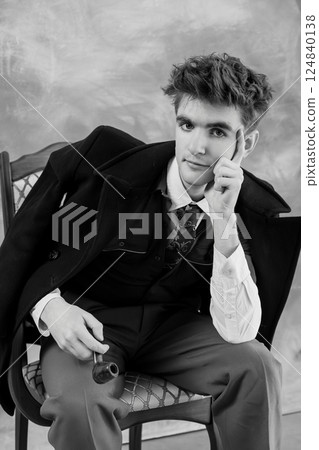 Black and white portrait of a young man in formal attire, seated with a thoughtful expression and holding a pipe Black and white portrait of a young man in formal attire, seated with a thoughtful expression and holding a pipe 124840138