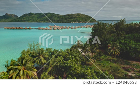 Breathtaking drone footage captures the idyllic beauty of Bora Bora, showcasing a luxurious overwater bungalow resort nestled amidst crystal-clear turquoise waters and lush tropical vegetation 124840558