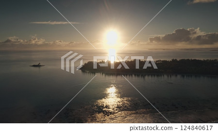 Golden sunlight reflects off serene waters as the sun sets behind an island. Perfectly captured from above, the sky transitions through warm hues, creating a peaceful atmosphere. 124840617