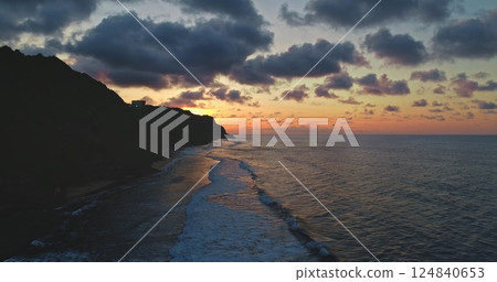 Golden hour sunlight reflecting on the ocean waves gently breaking on the shore and a dramatic cloudscape during sunset over a cliff in Bali, Indonesia Golden hour sunlight reflecting on the ocean waves gently breaking on the shore and a dramatic cloudscape during sunset over a cliff in Bali, Indonesia 124840653