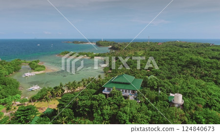Aerial view capturing a tropical resort with a green roof nestled in lush vegetation, overlooking the turquoise waters and coral reefs of Malapascua Island, Philippines 124840673