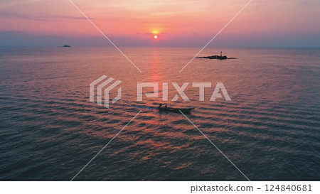 Aerial drone footage of a small fishing boat sailing on the calm sea during a beautiful sunset, with tropical islands and navigation signal in the background, creating a peaceful and scenic view 124840681
