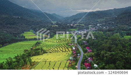 Stunning aerial view vibrant green rice terraces cascading down slopes, a winding road traversing the landscape, and a small village nestled in the mountains. Asia agriculture rural nature countryside Stunning aerial view vibrant green rice terraces cascading down slopes, a winding road traversing the landscape, and a small village nestled in the mountains. Asia agriculture rural nature countryside 124840694