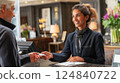 A female hotel receptionist smiling and handing a key card to a guest at upon check-in at the hotel counter in the lobby. Ai generated. 124840722