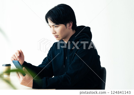A young man thinking by the window with his smartphone 124841143
