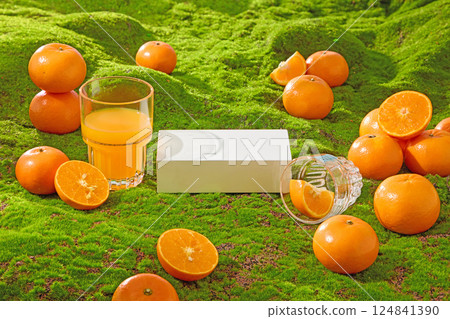 Rectangular empty pedestal placed in the middle of artificial grass. Ripe oranges cut in half to reveal fresh orange flesh and tiny orange seeds. Glasses placed horizontally next to the oranges. 124841390