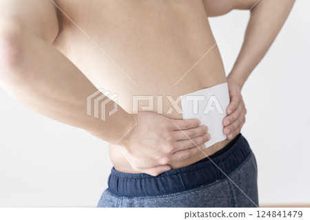 Man applying a compress to his lower back, lower back pain, compress, muscle pain Man applying a compress to his lower back, lower back pain, compress, muscle pain 124841479