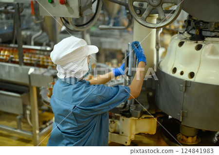 Factory worker in protective uniform adjusting industrial machinery in a canned fish processing plant 124841983
