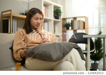 Female holding a glass of water and touching her cheek experiencing tooth sensitivity Female holding a glass of water and touching her cheek experiencing tooth sensitivity 124842013