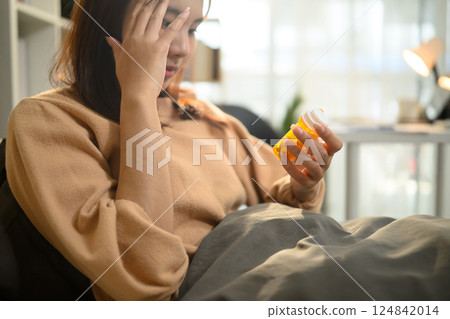 Young woman holding a bottle of medicine while suffering from illness Young woman holding a bottle of medicine while suffering from illness 124842014