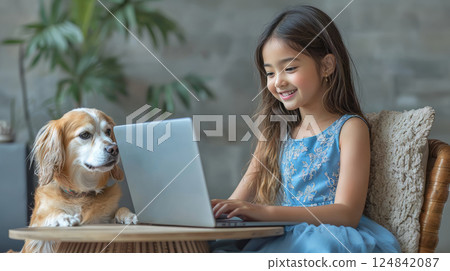 Smiling indian asian girl in beautiful light blue dress is making his homework with laptop on the table at home with her dog. Childhood and technology Smiling indian asian girl in beautiful light blue dress is making his homework with laptop on the table at home with her dog. Childhood and technology 124842087