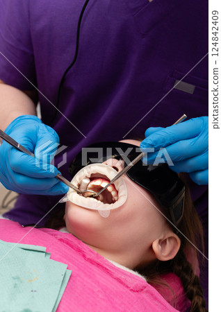 Young child receiving dental treatment with a calm expression in a modern clinic, surrounded by professional equipment during a bright afternoon appointment Young child receiving dental treatment with a calm expression in a modern clinic, surrounded by professional equipment during a bright afternoon appointment 124842409