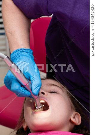 Child undergoing dental treatment in a bright clinic, focused on oral health while a dentist carefully works to ensure comfort and safety, surrounded by friendly atmosphere 124842420