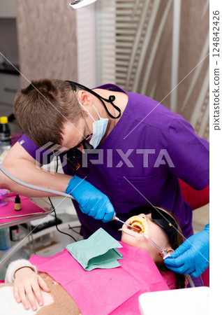 Dentist performs a delicate tooth procedure on a young patient in a modern dental clinic while maintaining a calming atmosphere on a sunny afternoon Dentist performs a delicate tooth procedure on a young patient in a modern dental clinic while maintaining a calming atmosphere on a sunny afternoon 124842426